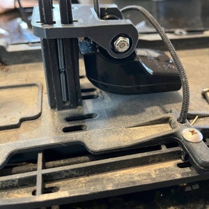 May include: A black plastic device with a small black cord attached. The device has a small black screw on the side and a black plastic arm that can be adjusted.