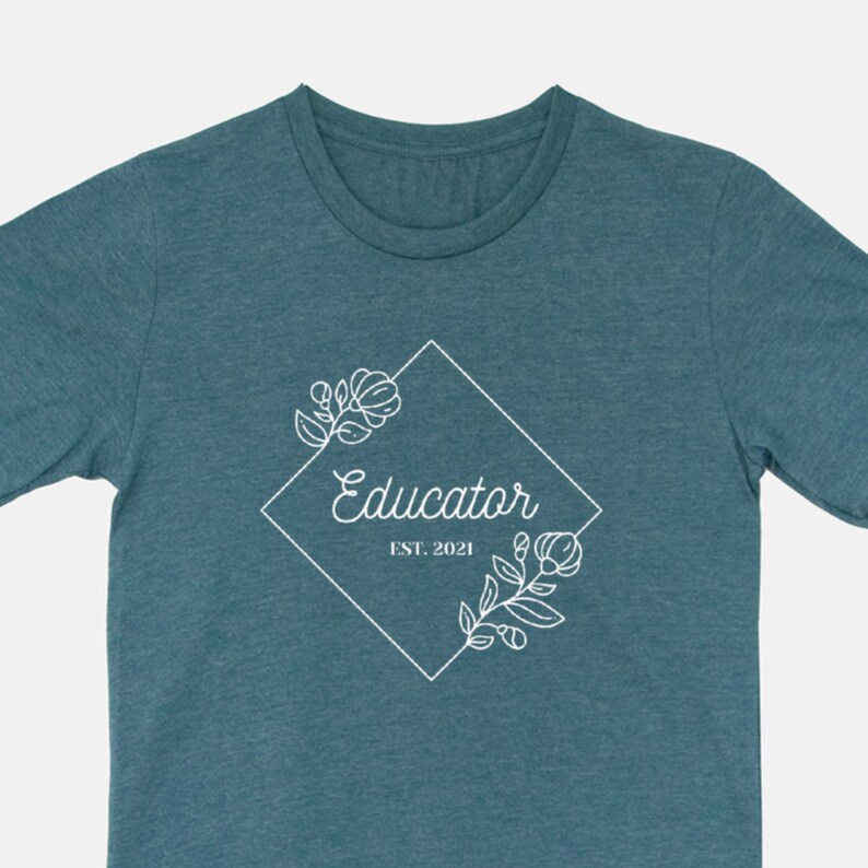 Puede incluir: Camiseta azul turquesa con un dise&ntilde;o gr&aacute;fico blanco de un marco de diamante con detalles florales y el texto "Educator Est. 2021".
