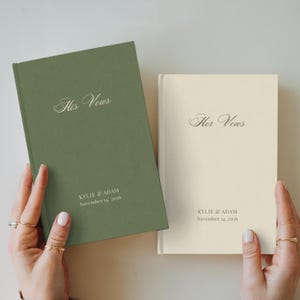 May include: Two hardcover vow books with a matte finish. The left book is sage green with the text His Vows, Kylie & Adam, and November 14, 2026. The right book is cream with the text Her Vows, Kylie & Adam, and November 14, 2026.