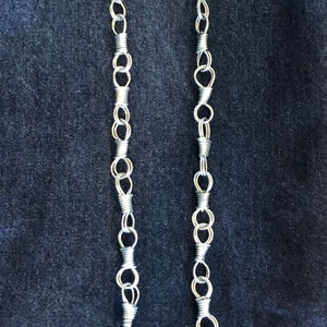 Puede incluir: Dos cadenas plateadas con un bucle en cada extremo. Las cadenas están hechas de múltiples anillos pequeños unidos.