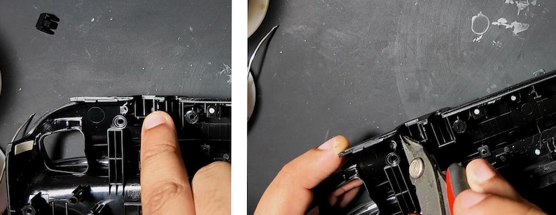 May include: Close-up of a person's finger pointing at a black plastic component. The component is part of a larger black device, possibly a game console or electronic gadget. A small black piece is detached.
