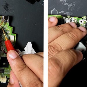 May include: Close-up of a circuit board being tested with red and black probes. The board is green with various components and connectors. The probes are held by hands, suggesting a repair or diagnostic process. The background is a dark surface.