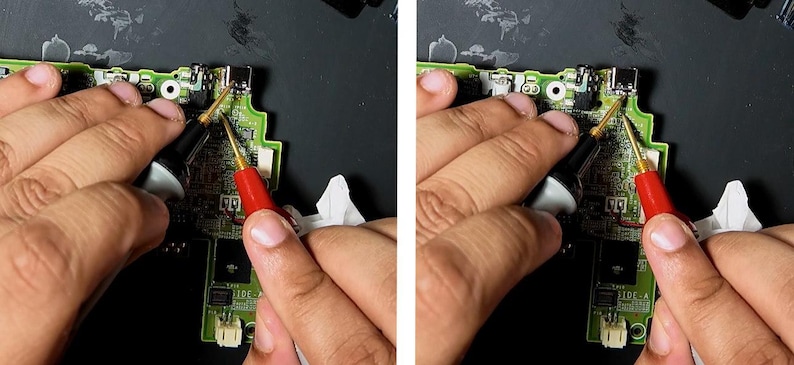 May include: Close-up of a circuit board being tested with red and black probes. The board is green with various components and connectors. The probes are held by hands, suggesting a repair or diagnostic process. The background is a dark surface.
