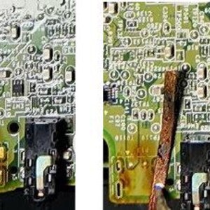 May include: Close-up of a green circuit board with various electronic components. The board has a black audio jack and several small, silver-colored components. There is a brown, rectangular object partially obscuring the board.