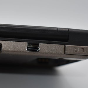 Puede incluir: Primer plano de un dispositivo de juego portátil negro y plateado con un puerto USB-C y un botón etiquetado como "L1".