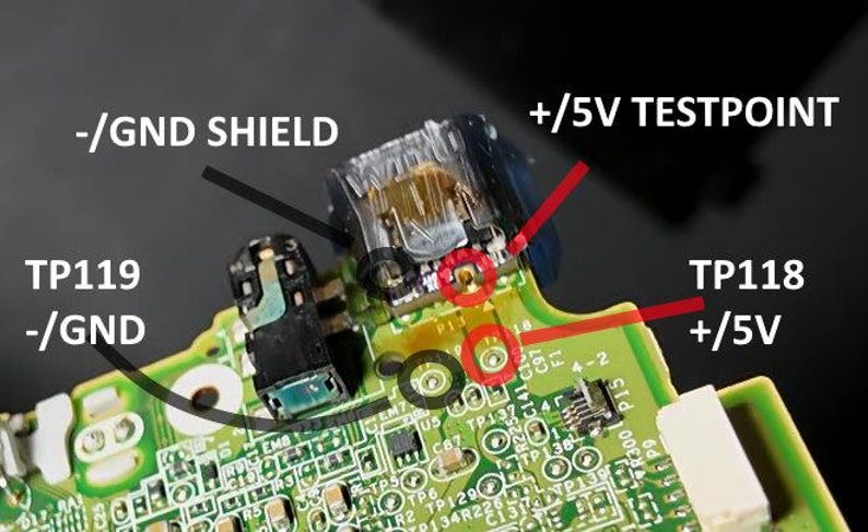 May include: Close-up of a circuit board with various components and text labels. Key labels include "-/GND SHIELD", "+/5V TESTPOINT", "TP119 -/GND", and "TP118 +/5V". Red circles highlight specific points on the board.