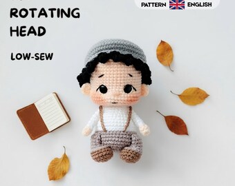 Könnte beinhalten: Eine Häkelpuppe mit schwarzen Haaren, einer grauen Mütze, einem weißen Hemd und einer grauen Hose mit braunen Schuhen. Der Text lautet 360 ROTATING HEAD, LOW-SEW und CROCHET PATTERN ESPAÑOL ENGLISH. Die Puppe ist von vier braunen Herbstblättern und einem kleinen Notizbuch umgeben.
