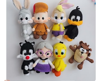 May include: A collection of handmade crochet dolls featuring cartoon characters, including Bugs Bunny, Daffy Duck, and Sylvester the Cat. Each doll is intricately crafted with detailed features and vibrant colors, showcasing a variety of outfits and expressions. The dolls are arranged on a white surface.