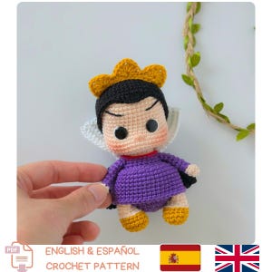 May include: A small crocheted doll featuring a black hair style, a yellow crown, and a purple dress. The doll has large black eyes, a light skin tone, and a white collar. The figure is crafted with visible yarn stitches and has yellow feet.
