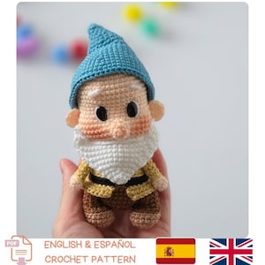 May include: A small, handmade crochet gnome doll featuring a pointed blue hat, a large white beard, a peach-colored face with black eyes, a yellow tunic with a black belt, and brown trousers. The figure is crafted with visible yarn stitches.