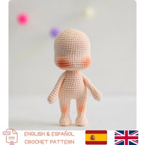 Peut inclure: Un corps de poupée crocheté de couleur pêche clair, avec des joues roses. La poupée a une tête arrondie, de petits bras et des jambes. L'image comprend également le texte "ENGLISH & ESPAÑOL CROCHET PATTERN" et les drapeaux de l'Espagne et du Royaume-Uni.