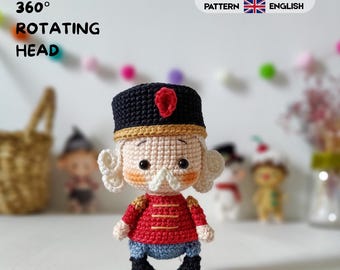 May include: A crocheted nutcracker doll featuring a black hat with a red accent, a red jacket with gold detailing, blue trousers, and black boots. The doll has white hair, a white mustache, and rosy cheeks. Text reads 360 ROTATING HEAD.