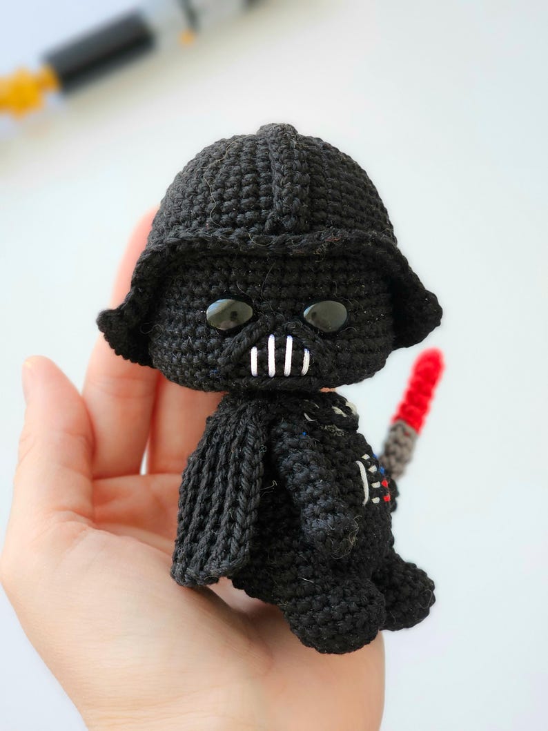 May include: A handmade black crochet Darth Vader doll with a red lightsaber. The doll features a detailed helmet, cape, and iconic facial features. The doll is approximately 4 inches tall.