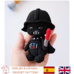 May include: A black crochet Darth Vader figure with a red lightsaber. The figure has a detailed helmet and chest plate. The image includes the text "ENGLISH & ESPA&Ntilde;OL CROCHET PATTERN".