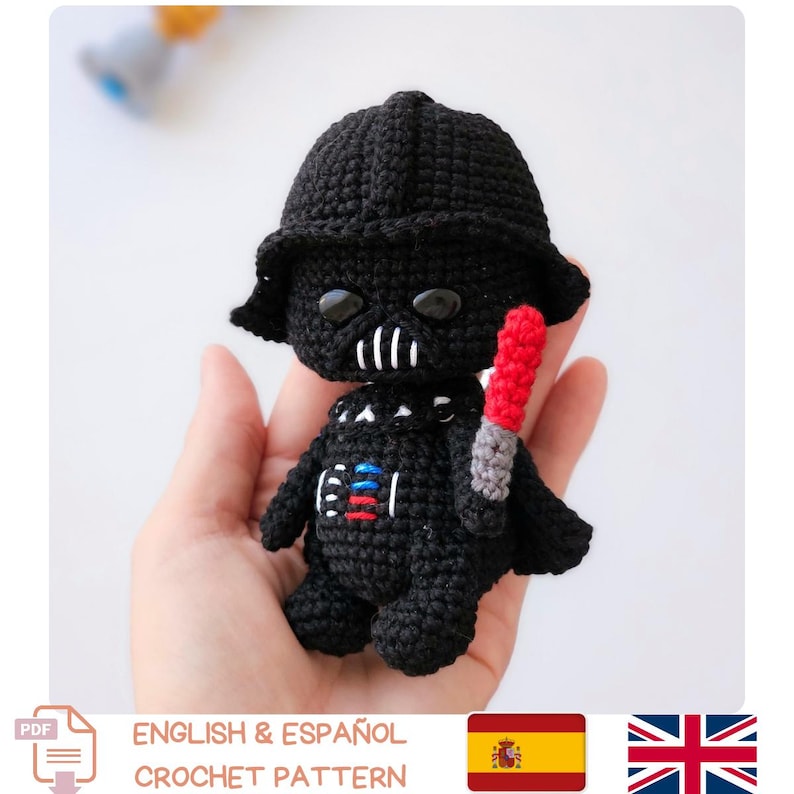 May include: A black crochet Darth Vader figure with a red lightsaber. The figure has a detailed helmet and chest plate. The image includes the text "ENGLISH & ESPA&Ntilde;OL CROCHET PATTERN".