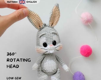 Könnte beinhalten: Eine gehäkelte Hasenpuppe in Grau und Weiß mit langen Ohren, schwarzen Augen und rosa Wangen. Der Text lautet: CROCHET PATTERN ESPAÑOL ENGLISH, 360° ROTATING HEAD und LOW-SEW. Der Hase hat einen hellgrauen Körper mit einem weißen Bauchfleck.