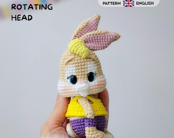 Könnte beinhalten: Eine gehäkelte Kaninchenpuppe mit beigem Fell, rosa gefütterten Ohren und einer gelben Haartolle. Das Kaninchen trägt ein gelbes Oberteil und eine violette Hose. Der Text lautet 360 ROTATING HEAD und CROCHET PATTERN ESPAÑOL ENGLISH.