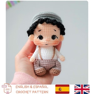 Könnte beinhalten: Handgefertigte Häkelpuppe mit grauer Mütze, schwarzen Haaren und einem weißen Hemd mit Hosenträgern. Die Puppe hat einen hellen Hautton und trägt braune Hosen und Schuhe. Der Text "ENGLISH & ESPAÑOL CROCHET PATTERN" ist enthalten.