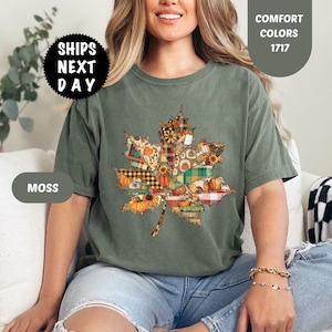 Puede incluir: Camiseta verde musgo con un diseño de hoja de arce colorida. La hoja está compuesta por varios patrones otoñales, incluyendo cuadros, girasoles y calabazas. La camiseta tiene el texto "COMFORT COLORS 1717" y "SHIPS NEXT DAY".