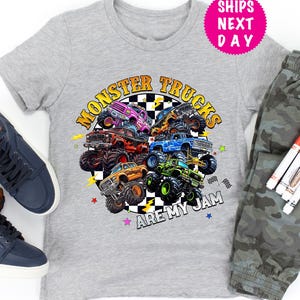 May include: A gray t-shirt with a colorful graphic of monster trucks and the text "Monster Trucks Are My Jam." The image also includes a pair of blue sneakers, camouflage pants, and markers.