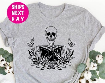 Pode incluir: Camiseta cinza com um esqueleto preto segurando um livro e rodeado de folhas.