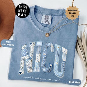 May include: A blue jean-colored t-shirt with the letters "NICU" in a faux patchwork design. The shirt has a crew neck and short sleeves. The text "neonatal intensive care unit" is printed below the letters. A gold necklace with a pendant is draped on the shirt.
