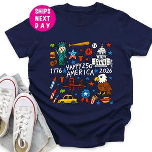 Puede incluir: Camiseta azul marino con un gr&aacute;fico colorido que celebra el 250 aniversario de Am&eacute;rica. El dise&ntilde;o incluye la Estatua de la Libertad, un bate de b&eacute;isbol, una pelota de baloncesto, el Capitolio y el texto "Happy 250 America 2026".