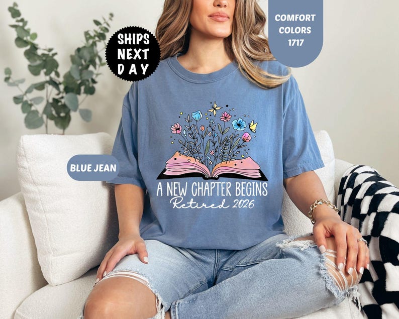 May include: Blue jean colored t-shirt with the text "A New Chapter Begins Retired 2026". The shirt features a graphic of an open book with flowers and butterflies. The shirt is a comfort color.