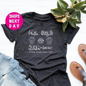 May include: Black t-shirt with white text that reads "Ms. Day's JAM-boree Sixth Grade Class, 2023". The text is surrounded by three drawings of jars with lids.