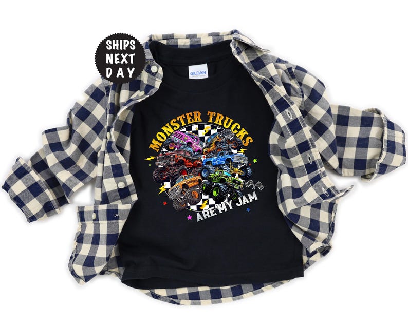 May include: Black t-shirt with a colorful graphic of monster trucks and the text "MONSTER TRUCKS ARE MY JAM". The shirt is layered with a blue and white plaid button-down shirt.