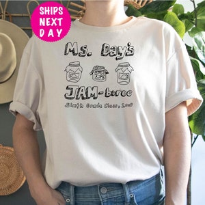 May include: White t-shirt with black text that reads "Ms. Day's JAM-boree Sixth Grade Class, 2023". The text is surrounded by three drawings of jars with lids.