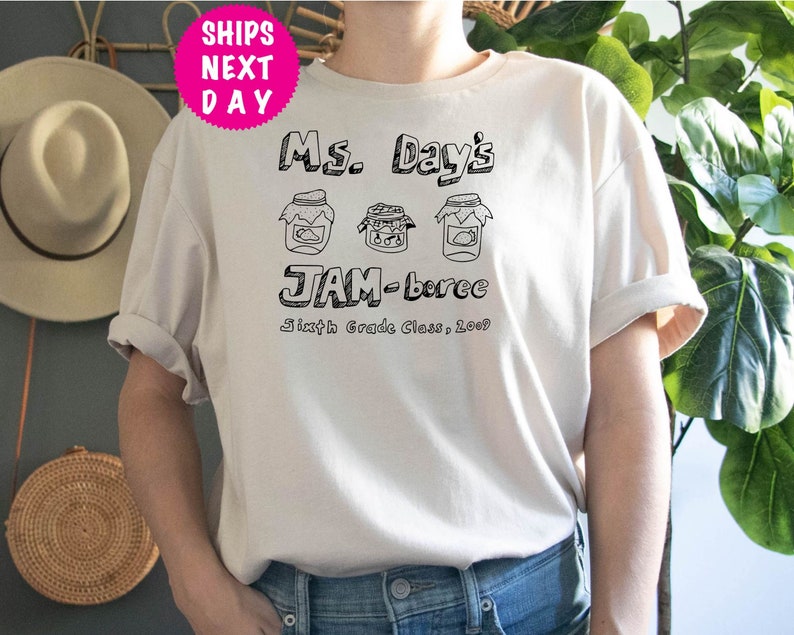 May include: White t-shirt with black text that reads "Ms. Day's JAM-boree Sixth Grade Class, 2023". The text is surrounded by three drawings of jars with lids.