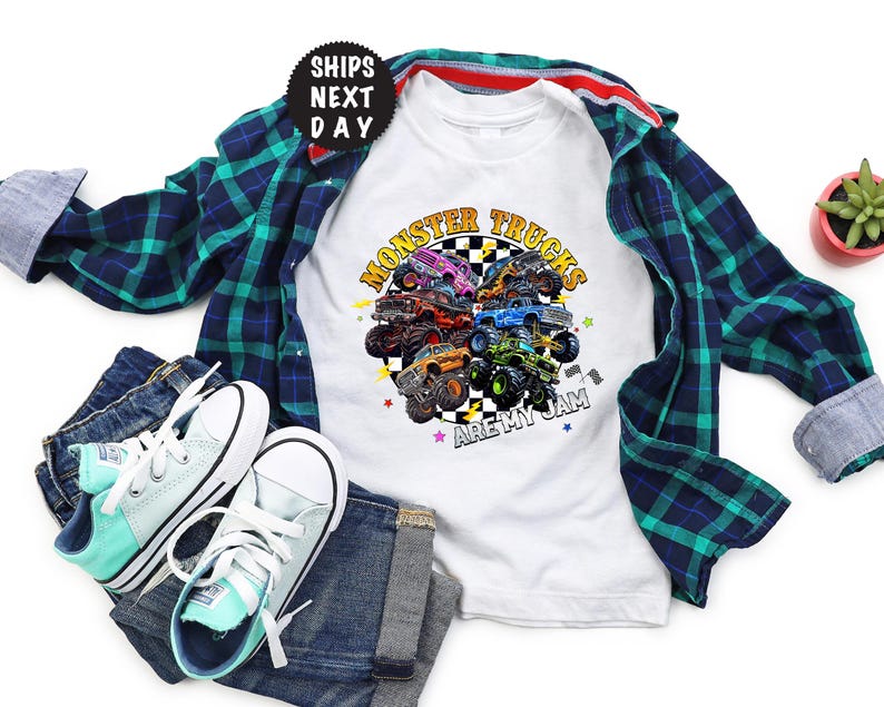 May include: White t-shirt with a colorful graphic of monster trucks and the text "Monster Trucks Are My Jam." The shirt is paired with a blue and green plaid shirt, blue jeans, and mint green and white sneakers.