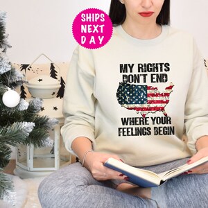 Op de afbeelding: Een wit sweatshirt met een verweerd Amerikaans vlagontwerp en de tekst "Mijn rechten eindigen niet waar jouw gevoelens beginnen".