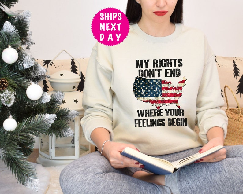 Op de afbeelding: Een wit sweatshirt met een verweerd Amerikaans vlagontwerp en de tekst "Mijn rechten eindigen niet waar jouw gevoelens beginnen".