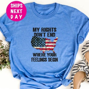 Op de afbeelding: Een blauw T-shirt met een verweerde Amerikaanse vlag afbeelding en de tekst "Mijn rechten eindigen niet waar jouw gevoelens beginnen".