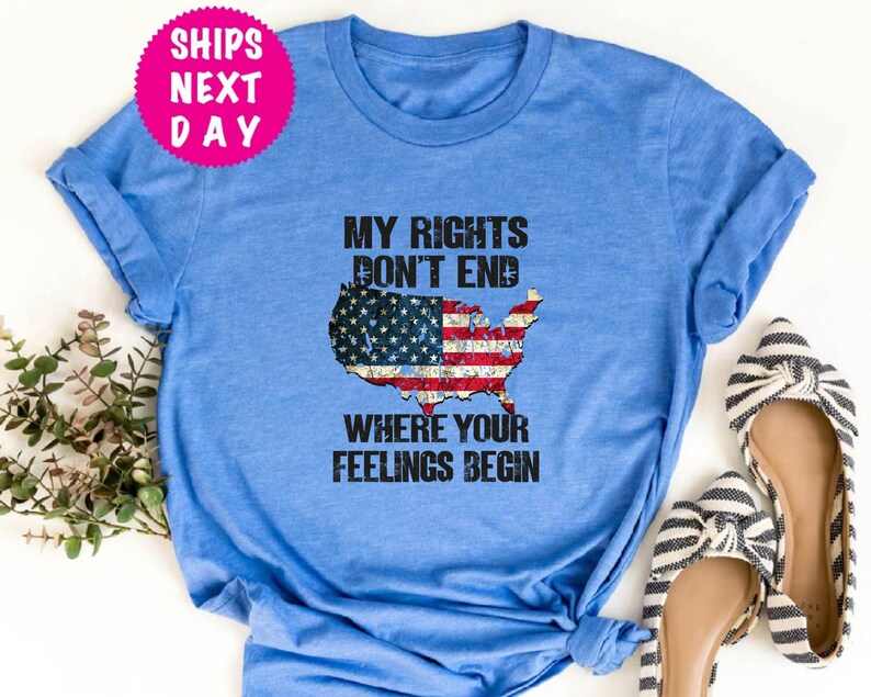Op de afbeelding: Een blauw T-shirt met een verweerde Amerikaanse vlag afbeelding en de tekst "Mijn rechten eindigen niet waar jouw gevoelens beginnen".