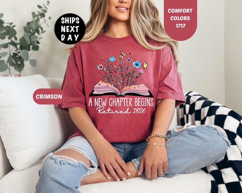 May include: Crimson-colored t-shirt with the text "A New Chapter Begins Retired 2026" and a graphic of an open book with flowers and butterflies. The shirt is a comfort color.