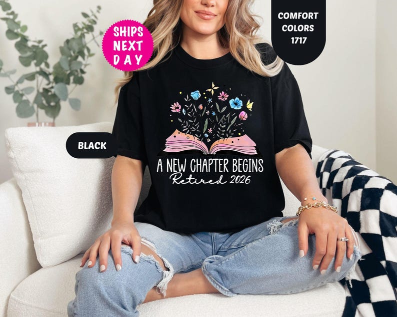 May include: Black t-shirt with the text "A NEW CHAPTER BEGINS Retired 2026" and a graphic of an open book with flowers. The shirt has a round neckline and short sleeves. The shirt is part of the "Comfort Colors" collection.