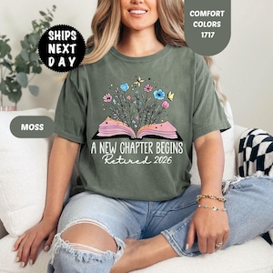 May include: Moss green t-shirt with the text "A NEW CHAPTER BEGINS Retired 2026". The graphic features an open book with flowers and butterflies. The shirt is a comfort color.