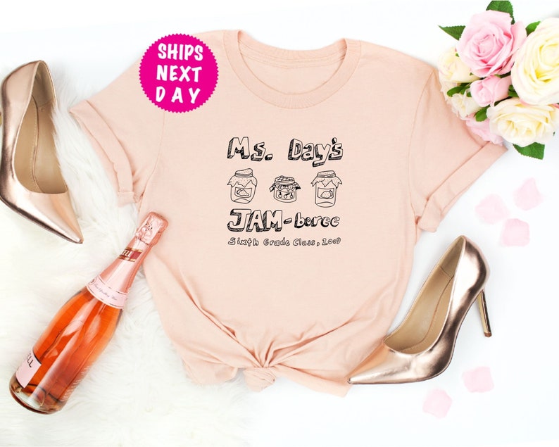 May include: A light pink t-shirt with black text that reads "Ms. Day's Jam-boree Sixth Grade Class, 2023". The text is surrounded by three drawings of jars with lids.