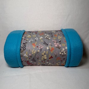Könnte beinhalten: Ein zylindrisches Kissen mit grau-weißem Blumenmuster und türkisfarbenem Fleece an den Enden.