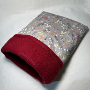 Peut inclure: Un coussin rectangulaire avec un motif floral gris et une bordure rouge foncé. Le tissu présente de petites fleurs roses, jaunes et oranges. La bordure rouge est en matière unie et douce.
