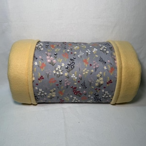 Puede incluir: Una cama cilíndrica para mascotas con estampado floral gris y blanco y forro de lana amarilla.