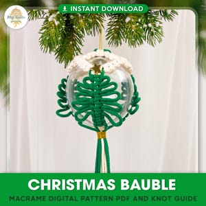 May include: A green macrame Christmas tree ornament inside a clear glass bauble with a white crocheted top. The ornament is hanging from a green and white cord.