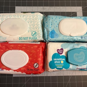 May include: Four packs of baby wipes in various colours are shown. The packs have plastic openings for easy access to the wipes. The text "DO NOT FLUSH" is printed on each pack. The red pack is 17.5cm x 18.8cm.