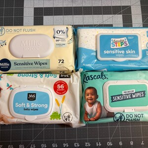 May include: Four packages of baby wipes are displayed. The brands include Millie Moon, Gentle Steps, 365, and Rascals. The packages are various colors, including yellow, blue, and green. Each package has a label indicating the number of wipes and the type, such as "sensitive skin."
