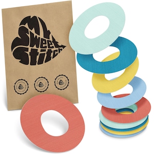 May include: A stack of colorful, textured, oval-shaped adhesive patches in shades of blue, yellow, and red. A brown paper package with the text "My Sweet Stitch" and three small circular logos is visible in the background.