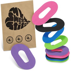 May include: A selection of oval-shaped adhesive patches in various colours: pink, black, blue, green, and purple. A brown paper bag with the text "My Sweet Stitch" in a heart shape is on the left, with three small circular logos.
