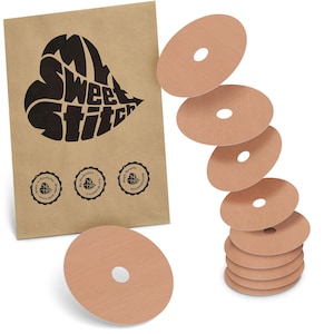 Puede incluir: Un paquete de papel marrón con un logotipo negro en forma de corazón con la inscripción "My Sweet Stitch", y varias cubiertas de pezones circulares de color beige con un agujero central. El paquete tiene tres sellos circulares.